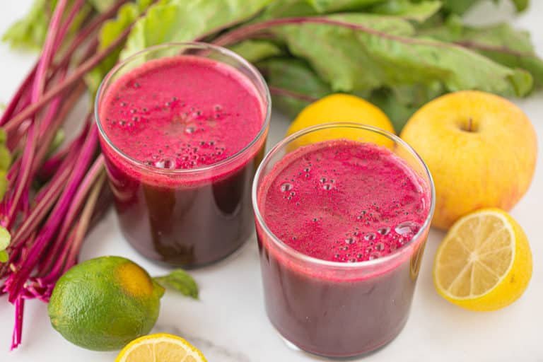 Deux verres de jus de betterave fait maison, entouré de citrons et de feuilles de betterave.