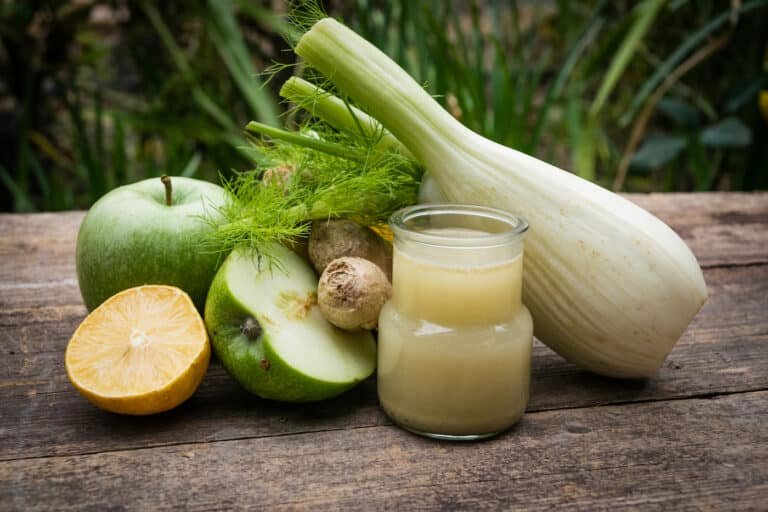 Un verre de jus de fenouil à côté du fenouil, de la pomme et du gingembre.