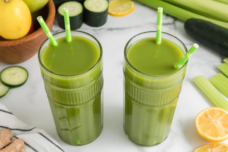 Deux grands verres de jus vert au citron et au gingembre, chacun avec deux pailles.