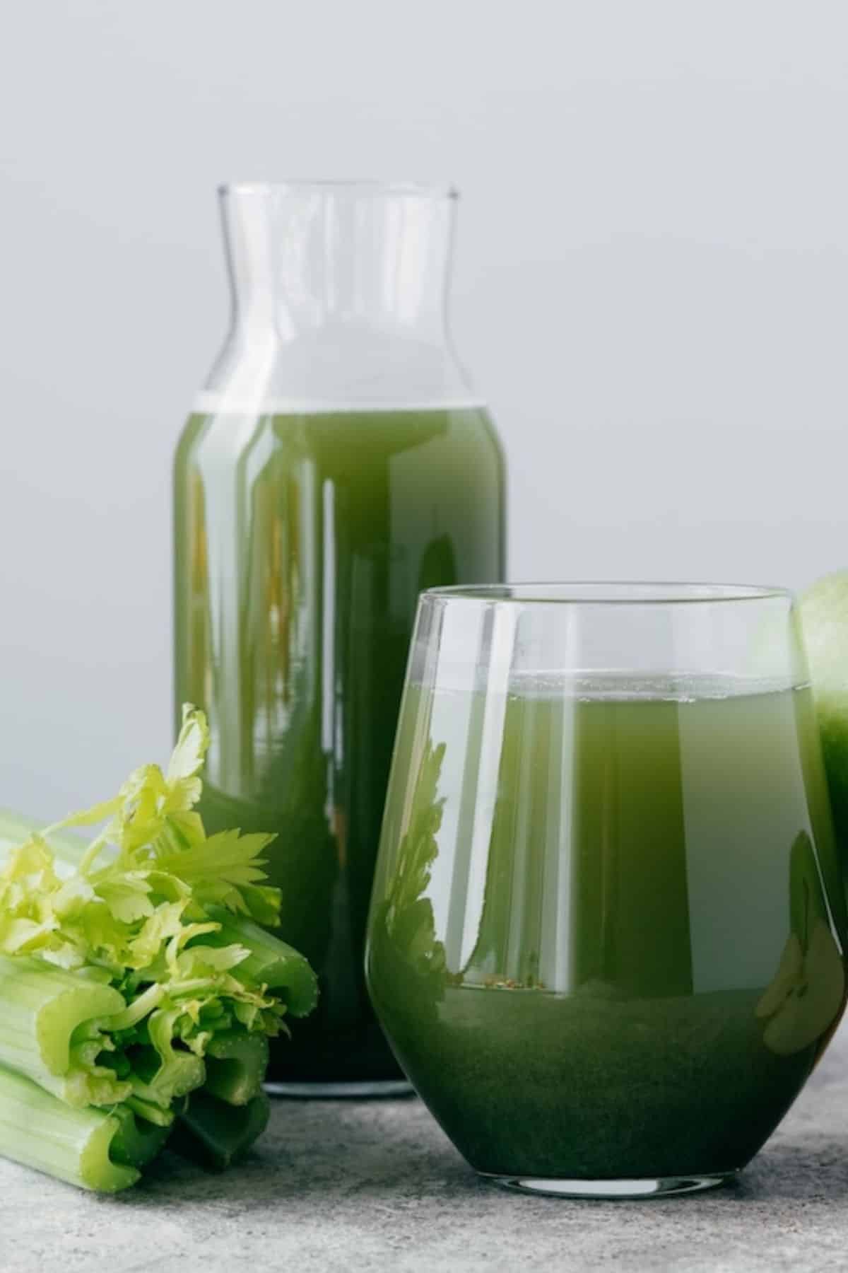 jus vert dans un pichet et un verre sur la table avec des fruits frais.