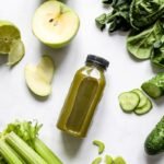 Flatlay of fresh green juice with vegetables and fruits on a white background, perfect for healthy lifestyle concepts.